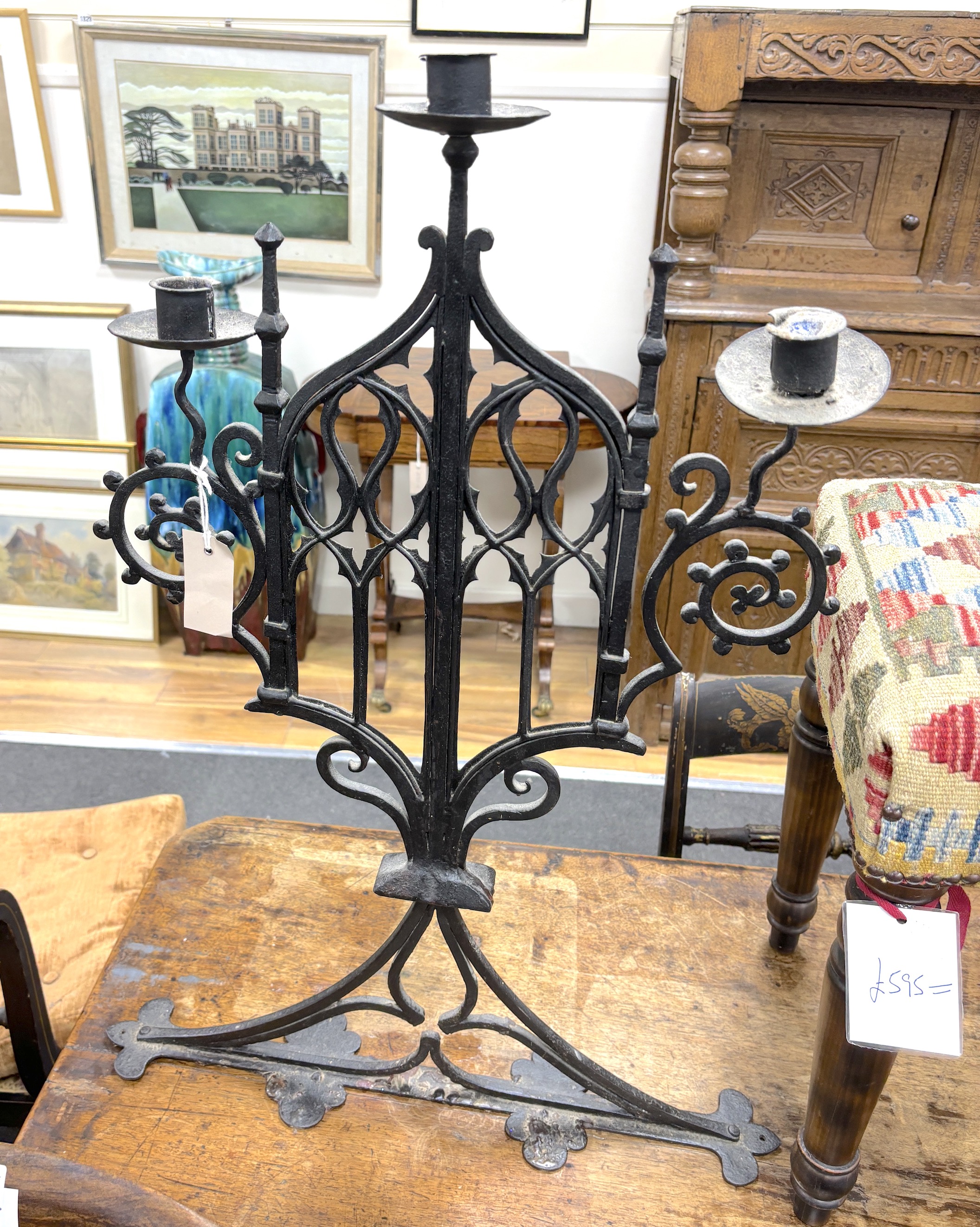 A pair of Gothic wrought iron three light candelabra, width 46cm, height 76cm, Provenance- Brede Place chapel, East Sussex, a former residence of the Frewen family from 1712-1936.